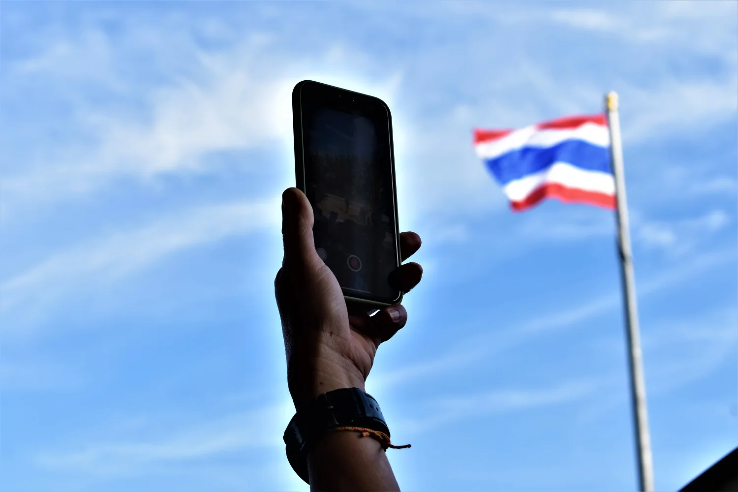 Hand eines Mannes hält Smartphone in den Himmel – beste mobile Internetgeschwindigkeit in Thailand mit AIS und DTAC erleben.