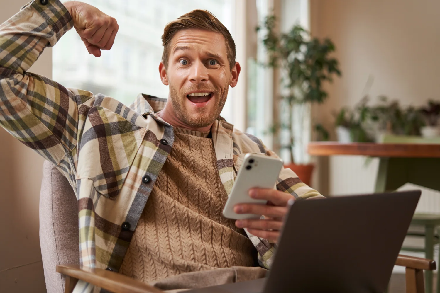 Sportlicher Mann zeigt Muskelpose im Café mit Laptop und Smartphone – genießt unbegrenztes Internet in Thailand dank eSIM.